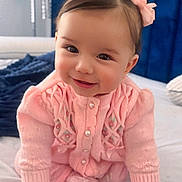 Emma Rose joined the competition — help win amazing prizes! baby, child, pink_clothing, bows, smiling, crawling, bed, blanket, headboard, indoor, cute, infant, knitted_sweater, happy, face, hands, portrait, person, young_child, home