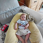 Tiago participe au concours pour gagner de l'argent avec cette photo : baby, child, couch, pillow, cushion, furniture, indoor, person, toddler, clothing, shorts, tshirt, wooden_cabinet, floor_tiles, electronic_device, power_strip, blanket, rug, relaxing, home