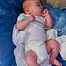 baby, sleeping, pacifier, blanket, white_clothing, infant, cozy, thumb_sucking, face, peaceful, soft_texture, child, resting, blue_blanket, wrapped, indoors, cute, newborn, comfort, relaxation