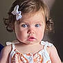 angel, baby, blue_eyes, bow, child, curious, curly_hair, cute, decor, footwear, indoor, infant, orange_pattern, person, portrait, romper, sitting, skin, toy, wall_decoration