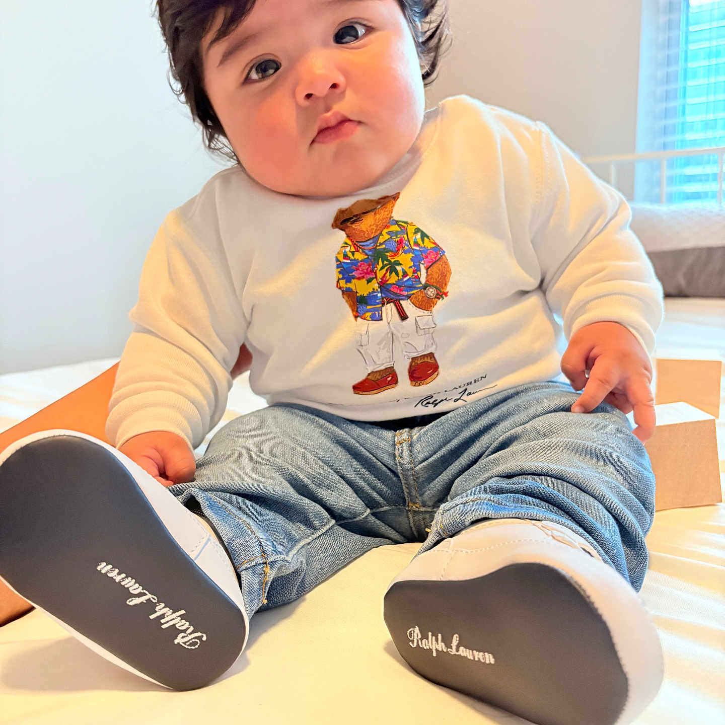 Danny Rodenas is registered to the contest to win money with this photo: adorable, baby, bed, child, clothing, cute, denim_pants, fashion, footwear, home, indoor, infant, natural_light, person, portrait, shoes, sitting, soft_light, white_sweater, window