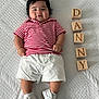 baby, child, infant, smiling, striped_shirt, white_shorts, white_shoes, wooden_blocks, name_blocks, lying_down, blanket, cute, indoors, person, portrait, playful, happy, chubby_cheeks, clothing, feet