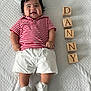 Danny Rodenas is registered to the contest to win money with this photo: baby, child, smiling, lying_down, striped_shirt, white_shorts, white_shoes, wooden_blocks, name_blocks, textured_blanket, happy, cute, infant, portrait, indoors, person, playful, young_child, clothing, footwear