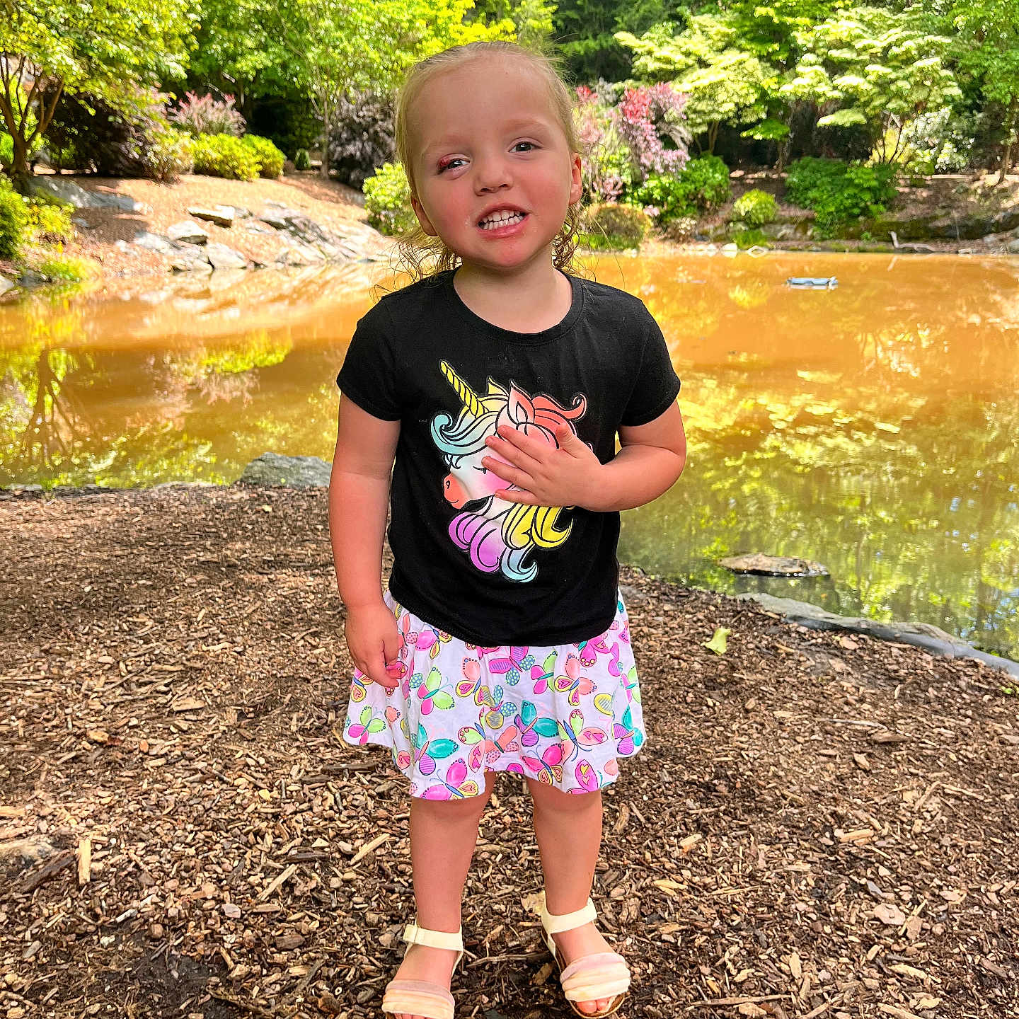 Layla King is registered to the contest to win money with this photo: child, cute, daylight, girl, greenery, happy, nature, outdoor, playful, pond, sandals, skirt, smiling, standing, summer, trees, tshirt, unicorn, woodchips, young