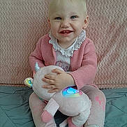 Shana a rejoint le concours — aidez-le/la à gagner de superbes lots ! baby, blanket, child, comfort, cute, earrings, face, happy, indoor, person, pigtails, pink_clothing, plush_toy, portrait, quilt, sitting, smiling, toddler, toy, unicorn