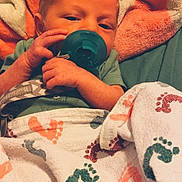 Rowan is registered to the contest to win money with this photo: baby, infant, child, portrait, sleepy, pacifier, blanket, swaddled, lying_down, face, eyes, hands, green_clothing, patterned_blanket, footprints, indoors, cozy, closeup, soft_lighting, adorable