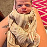newborn, baby, infant, child, portrait, face, eyes, striped_outfit, clothing, onesie, sitting, lap, adult, arms, tattoo, indoor, rug, cozy, photograph, serious_expression