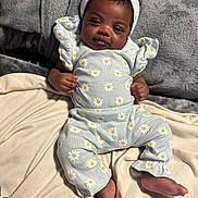 Karsyn is registered to the contest to win money with this photo: baby, infant, child, portrait, smiling, sitting, indoors, bed, blanket, headband, bow, floral_pattern, daisy, romper, clothing, cozy, bedroom, face, barefoot, photography