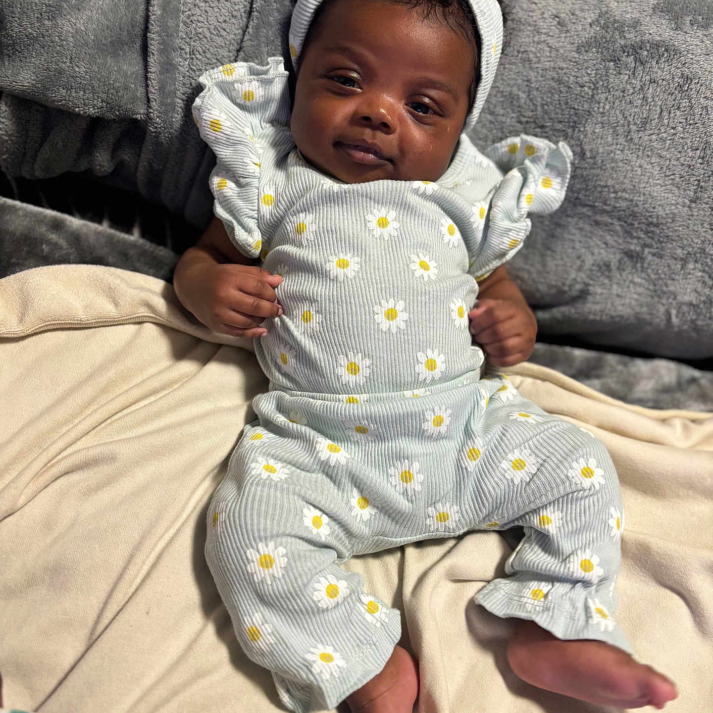 Karsyn is registered to the contest to win money with this photo: baby, infant, child, portrait, smiling, sitting, indoors, bed, blanket, headband, bow, floral_pattern, daisy, romper, clothing, cozy, bedroom, face, barefoot, photography