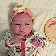 Samantha is registered to the contest to win money with this photo: baby, infant, headband, flower, onesie, animal_print, giraffe, lion, teddy_bear, pink, peach, hand, face, rosy_cheeks, blanket, quilted, wooden_plaque, lying_down, cute, portrait