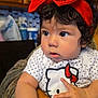 baby, child, face, headband, red_bow, hello_kitty, shirt, polka_dot, curly_hair, indoor, kitchen, person, cute, expression, arms, holding, portrait, infant, clothing, furniture