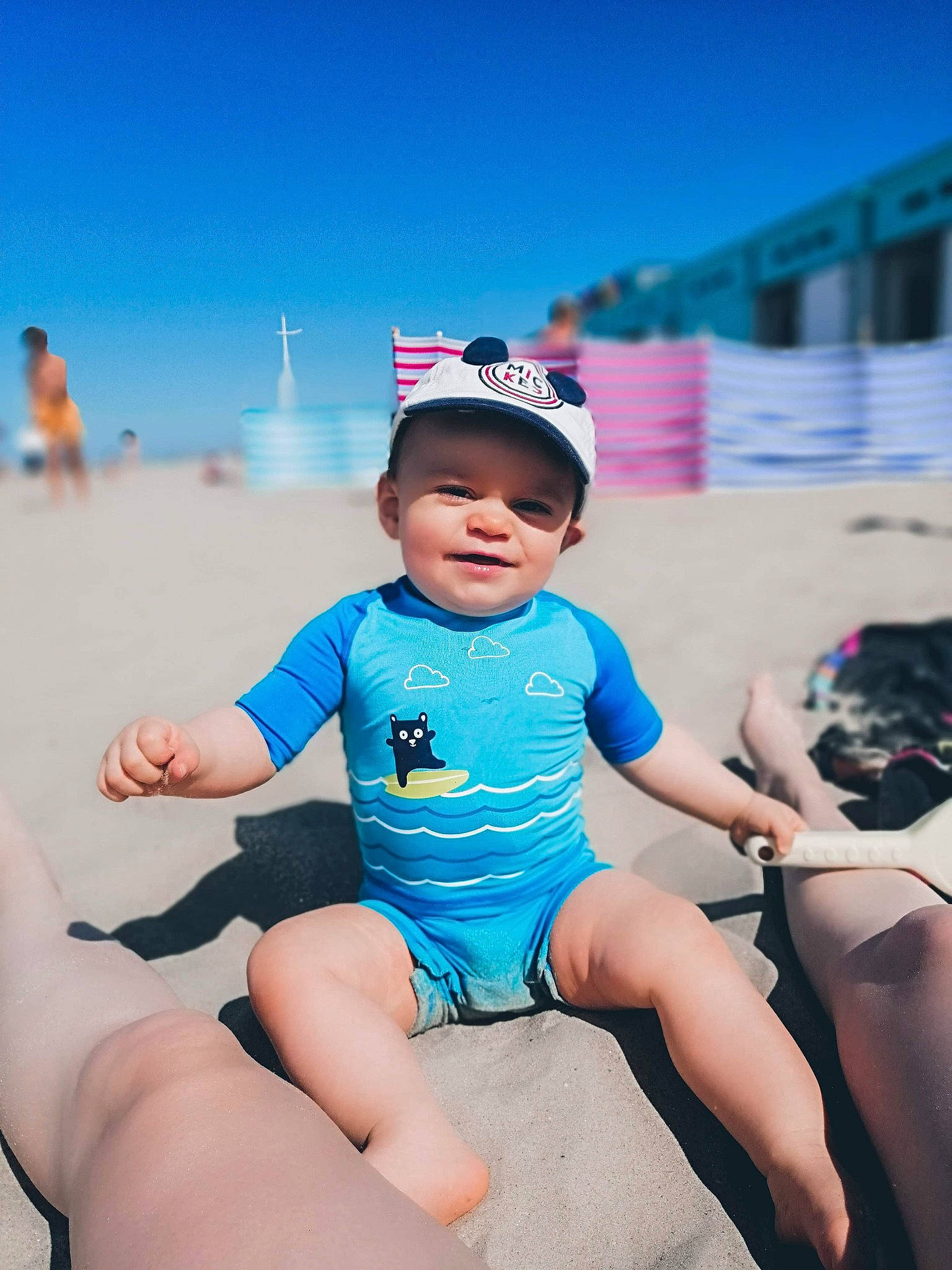 Timotë a rejoint le concours — aidez-le/la à gagner de superbes lots ! baby, beach, blue, child, fun, happy, headgear, headwear, leg, leisure, person, photography, sand, sea, sitting, skin, sky, snapshot, summer, toddler