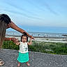 toddler, child, adult, beach, ocean, sky, concrete, grass, flowers, barefoot, smiling, holding_hands, casual_clothing, outdoor, nature, sunset, water, people, sand, happy