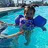 toddler, child, pool, water, floaties, swim_vest, pigtails, sunny, outdoor, summer, adult_hand, swimming, blue_water, recreation, leisure, vacation, smiling, happy, daytime, people