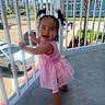 Tania joined the competition — help win amazing prizes! toddler, child, girl, pink_dress, pigtails, balcony, railing, barefoot, smiling, outdoor, daylight, parking_lot, cars, buildings, concrete_floor, person, happy, cute, hair, playful