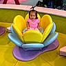 Tania joined the competition — help win amazing prizes! toddler, child, smiling, pink_clothing, flower_shaped_seat, colorful, indoor, play_area, soft_play, cushions, happy, hair_ponytail, playful, person, seat, flooring, yellow, blue, purple, green