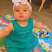 Mila participe au concours pour gagner de l'argent avec cette photo : baby, child, headband, bow, dress, toy, play_mat, floor, wooden_chair, indoor, colorful, alphabet, infant, sitting, cute, person, foot, hand, face, curious