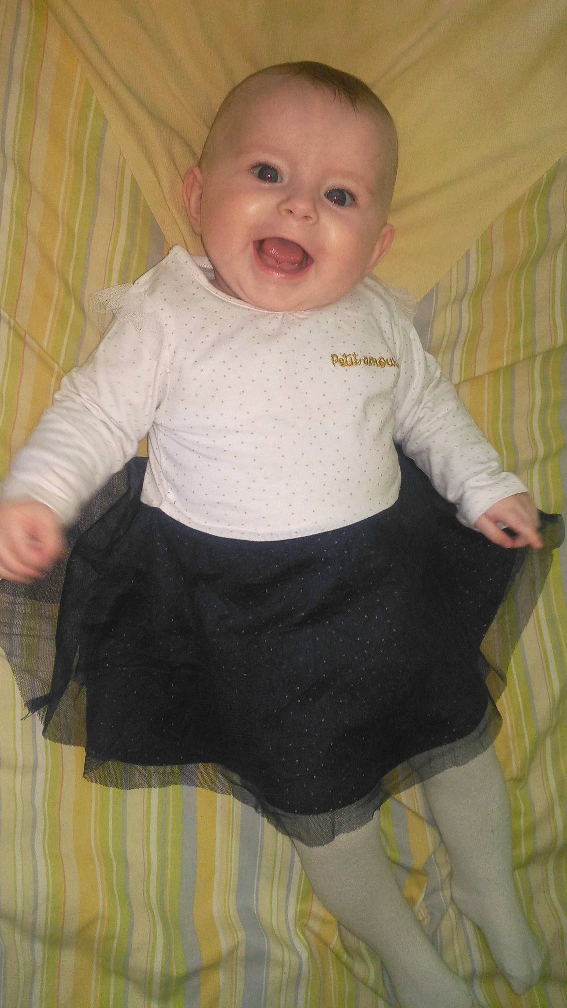 Léa participe au concours pour gagner de l'argent avec cette photo : arm, baby, baby_toddler_clothing, cheek, child, collar, eye, face, head, human_body, iris, neck, organ, pattern, person, product, sitting, sleeve, smile, t_shirt