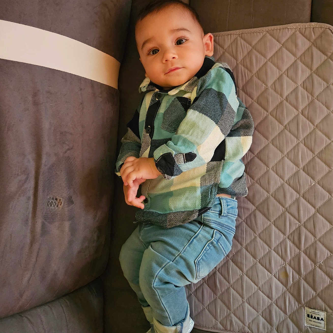 Melyan participe au concours pour gagner de l'argent avec cette photo : baby, casual_clothing, child, comfortable, couch, curious, cute, denim_jeans, fabric, home, indoor, infant, plaid_shirt, portrait, quilted_mat, relaxed, seated, sneakers, soft_lighting, young