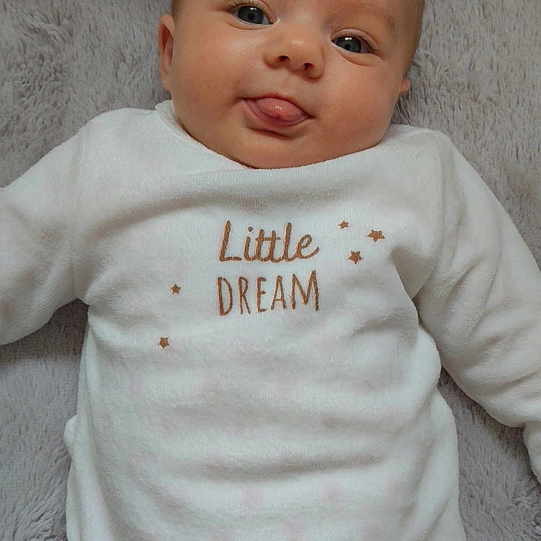 Luciana a rejoint le concours — aidez-le/la à gagner de superbes lots ! baby, blanket, child, close_up, cozy, cute, expression, eyes, face, head, indoors, infant, lying_down, playful, portrait, skin, smiling, soft_texture, tongue, white_clothing