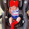 baby, infant, sleeping, car_seat, red_bow, red_socks, patriotic_outfit, blue_clothing, stars, white_clothing, portrait, close_up, indoors, adult_hand, safety_harness, headband, peaceful, nap, child, face