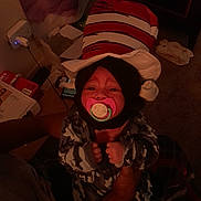 Winter joined the competition — help win amazing prizes! baby, pacifier, hat, striped_hat, child, infant, hands, person, indoor, dim_lighting, camouflage_clothing, carpet, box, power_outlet, blanket, furniture, toy, room, adult, holding