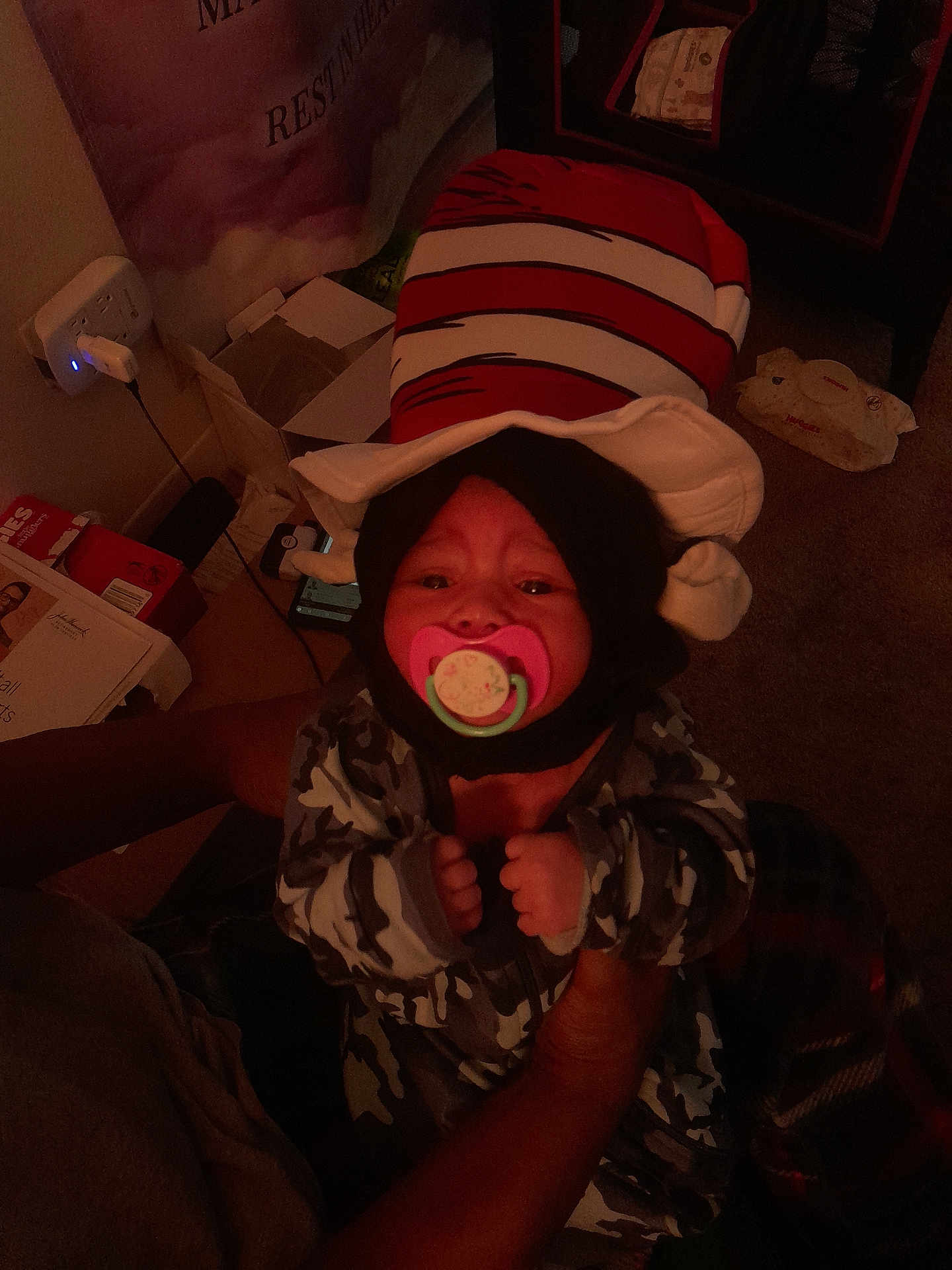 Winter joined the competition — help win amazing prizes! baby, pacifier, hat, striped_hat, child, infant, hands, person, indoor, dim_lighting, camouflage_clothing, carpet, box, power_outlet, blanket, furniture, toy, room, adult, holding