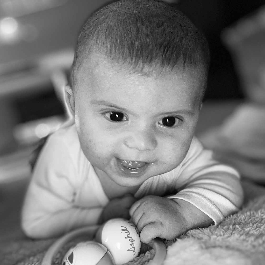 Jules a rejoint le concours — aidez-le/la à gagner de superbes lots ! baby, black_and_white, blanket, child, closeup, clothing, cute, expression, face, hand, happy, indoor, infant, lying_down, playful, portrait, skin, smiling, toy, young
