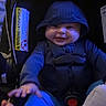 baby, child, car_seat, hood, smile, infant, happy, clothing, seatbelt, foot, hand, blue_pants, dark_background, indoor, safety, cute, young_child, infant_toy, child_seat, apparel