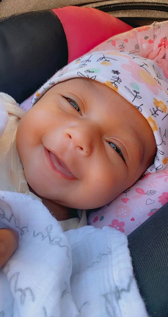 Nia is registered to the contest to win money with this photo: baby, cheek, chin, eye, eyebrow, eyelash, face, facial_expression, finger, happy, headwear, iris, joy, lip, nose, person, pink, skin, sleeve, smile