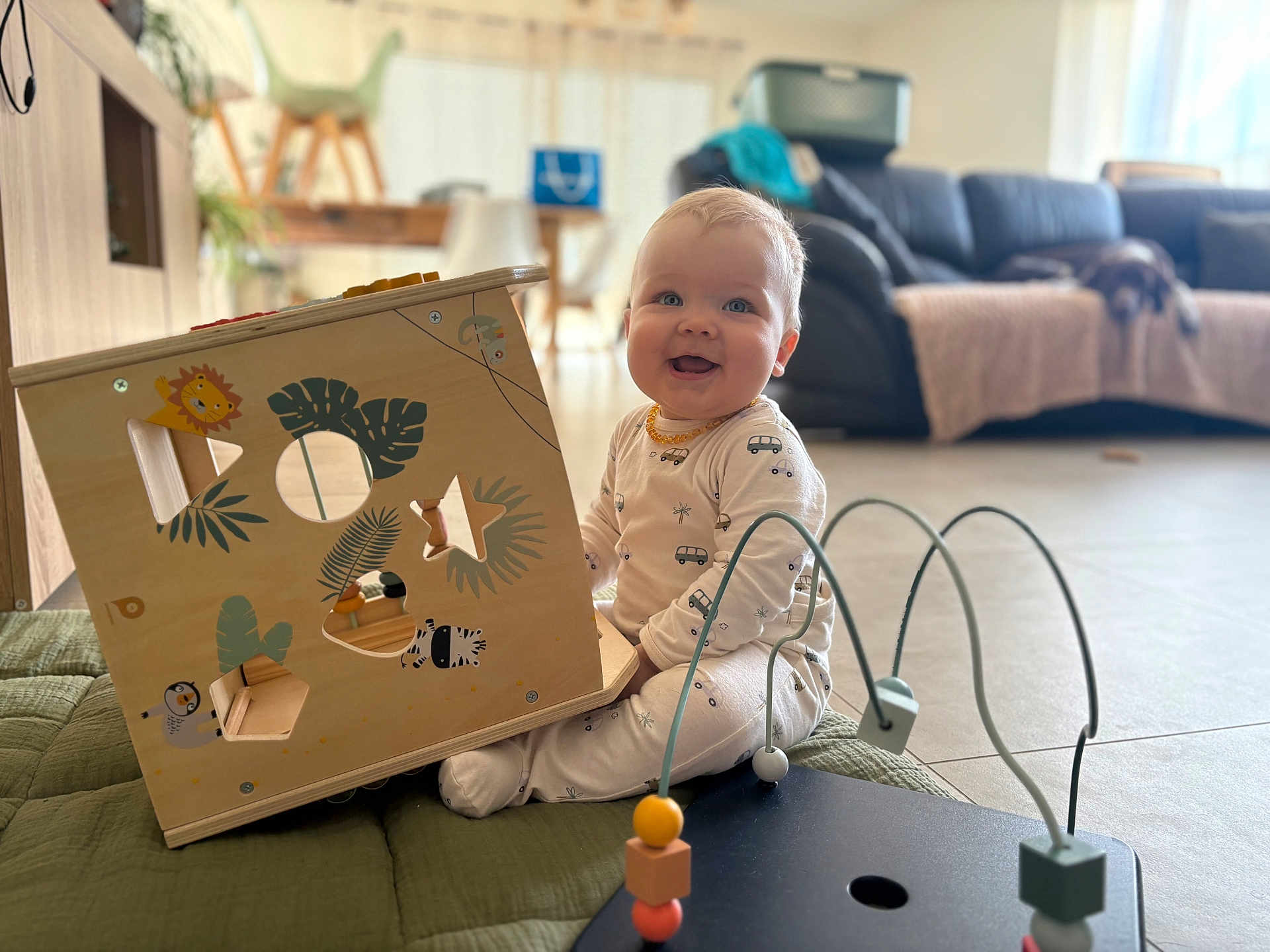 Léon a rejoint le concours — aidez-le/la à gagner de superbes lots ! baby, child, pajamas, toy_box, wooden_toy, bead_maze, indoor, living_room, couch, dog, floor, mat, smiling, playtime, furniture, animal_stickers, cute, happy, person, home