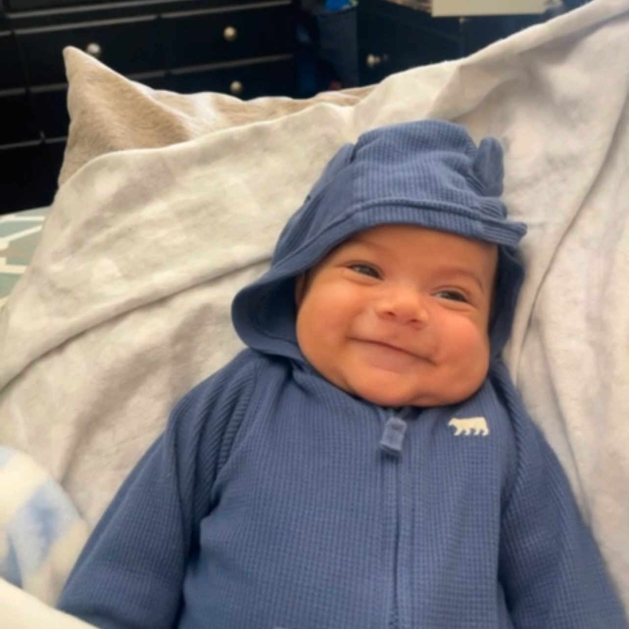 Aziel is registered to the contest to win money with this photo: baby, blanket, clothing, coat, face, furniture, happy, hat, head, hood, hoodie, jacket, knitwear, pants, person, photography, portrait, smile, sweater, sweatshirt