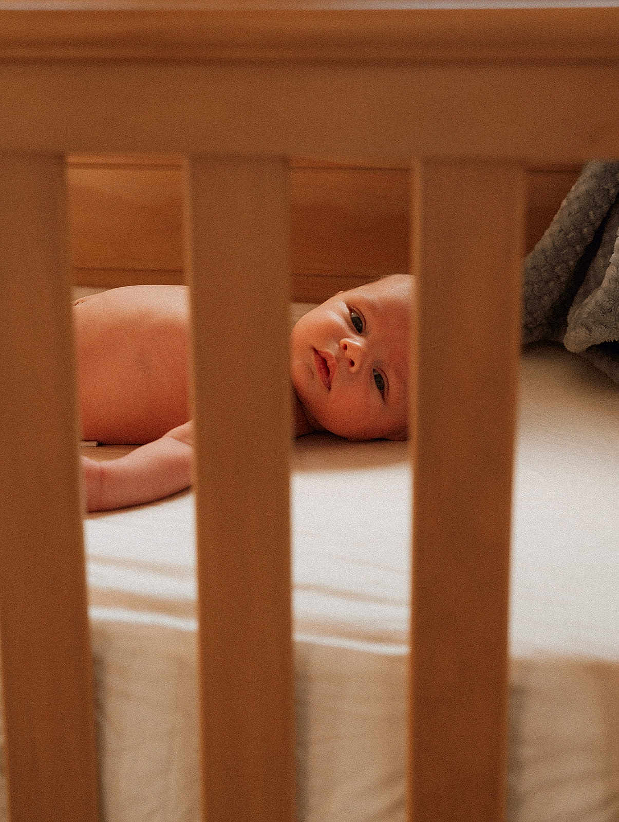 Coast joined the competition — help win amazing prizes! baby, infant, newborn, crib, crib_slats, wooden_crib, mattress, bedding, blanket, gray_blanket, lying_down, face, eyes, gaze, soft_light, warm_tones, portrait, closeup, nursery, candid