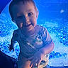 Nora joined the competition — help win amazing prizes! toddler, child, blue_light, water_bubbles, hand_holding, curious, indoor, short_sleeve_shirt, jeans, portrait, smile, face, baby, person, lighting, aquarium, background, candid, closeup, playful