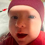 Nora is registered to the contest to win money with this photo: baby, close_up, face, hat, red_clothing, infant, expression, mouth_open, eyes, skin, headwear, indoors, portrait, child, cute, young, lying_down, soft_background, flower, cozy