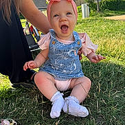 Isabella-Rayne is registered to the contest to win money with this photo: baby, child, smiling, happy, outdoor, grass, headband, bow, denim_overalls, socks, person, sunlight, nature, candid, sitting, supporting_hand, greenery, daylight, casual_clothing, infant