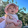 Isabella-Rayne is registered to the contest to win money with this photo: arm, baby, blue_sky, child, cute, daylight, floral_clothing, happy, holding, infant, nature, outdoor, person, portrait, smiling, summer, sunhat, sunshine, tattoo, trees