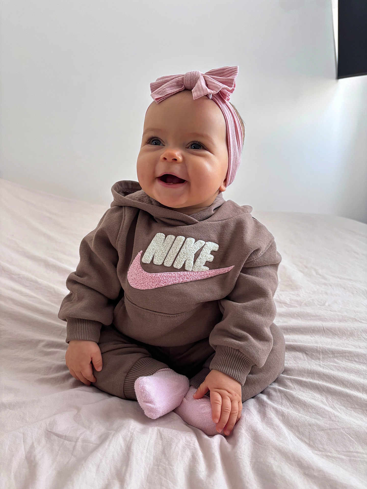 Inna participe au concours pour gagner de l'argent avec cette photo : baby, child, smile, hoodie, nike, pink_bow, headband, socks, bed, indoor, cute, happy, portrait, sitting, clothing, young_child, infant, cozy, person, apparel