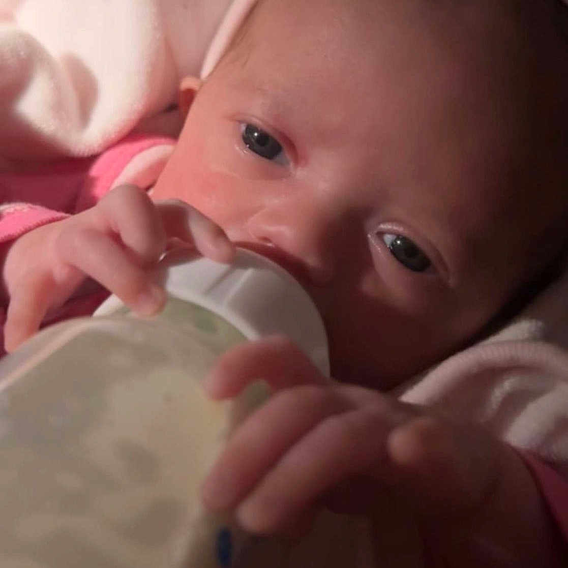 Zaza is registered to the contest to win money with this photo: baby, bottle, child, close_up, comfort, cute, feeding, hand, headband, indoor, infant, milk, newborn, person, pink_blanket, portrait, rest, sleeping_area, soft_toys, warm_lighting