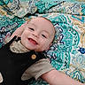 baby, smiling, infant, child, happy, lying_down, blanket, patterned, colorful, face, cute, clothing, striped_shirt, black_overall, indoors, portrait, young_child, closeup, cheerful, expression