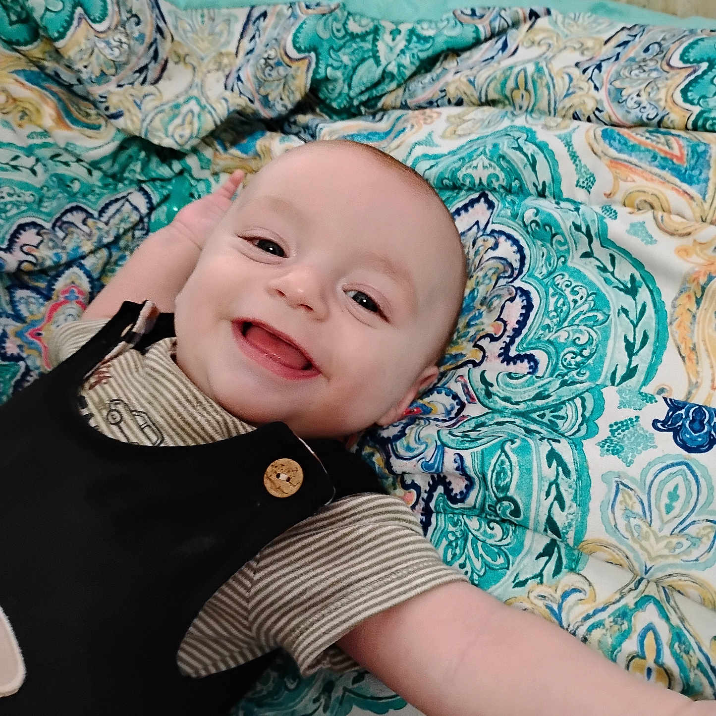 Bently joined the competition — help win amazing prizes! baby, smiling, infant, child, happy, lying_down, blanket, patterned, colorful, face, cute, clothing, striped_shirt, black_overall, indoors, portrait, young_child, closeup, cheerful, expression