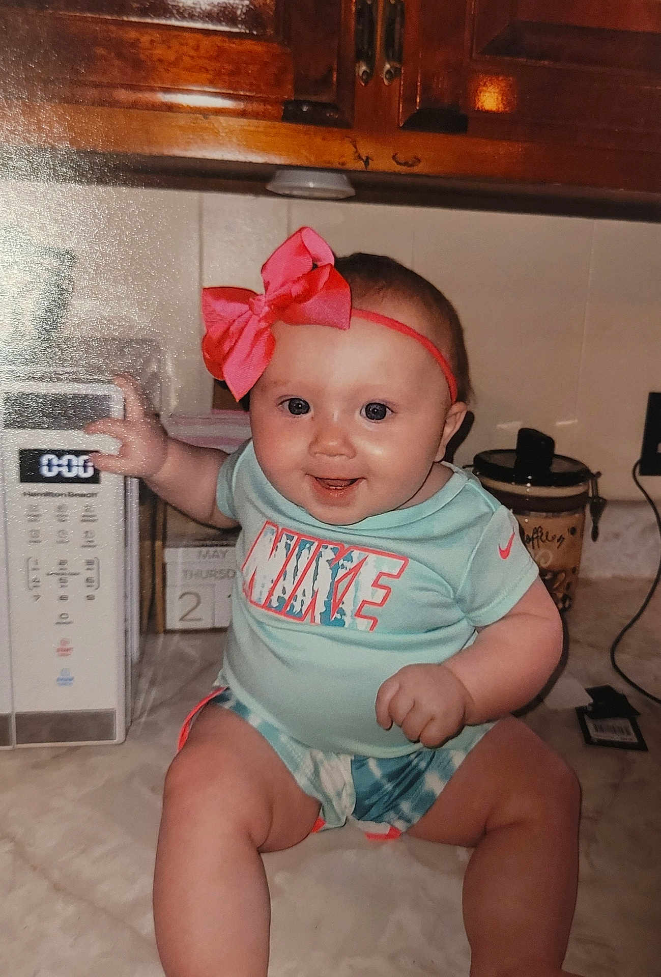 Emerie joined the competition — help win amazing prizes! baby, infant, child, smiling, sitting, kitchen, microwave, pink_bow, headband, nike, clothing, countertop, appliance, cabinet, happy, indoor, person, cute, playful, young