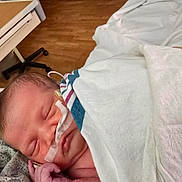 Arora joined the competition — help win amazing prizes! newborn, baby, sleeping, hospital, blanket, medical_tape, nasal_tube, gown, face, hand, infant, patient, healthcare, bed, wooden_floor, peaceful, resting, indoors, closeup, care