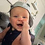 Bentley is registered to the contest to win money with this photo: baby, child, smiling, cap, hand, indoor, living_room, person, cute, happy, holding, fingers, casual, home, furniture, couch, drink, table, relaxed, portrait