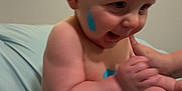 Bentley is registered to the contest to win money with this photo: baby, child, diaper, paint, blue_paint, smiling, sitting, bed, blanket, skin, face, hand, foot, window, blinds, indoor, cute, playful, person, infant