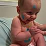 baby, child, diaper, paint, blue_paint, smiling, sitting, bed, blanket, skin, face, hand, foot, window, blinds, indoor, cute, playful, person, infant