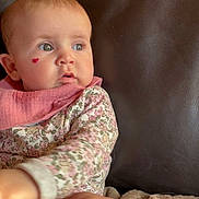 Mia participe au concours pour gagner de l'argent avec cette photo : baby, infant, heart_sticker, floral_clothing, pink_bib, blanket, leather_couch, curious, child, face, skin, eyebrows, cheek, sitting, indoors, soft_texture, comfort, young_child, portrait, expression