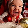 baby, infant, smiling, christmas, santa_hat, ornament, red, gold, holiday, decorations, close_up, face, blue_eyes, blanket, happy, mouth_open, festive, tree, toy, portrait