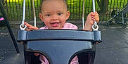 Mckenzie is registered to the contest to win money with this photo: toddler, swing, playground, child, smile, outdoor, park, greenery, chains, black_swing, sunlight, happy, grass, tree, pavement, stroller, person, clothing, feet, legs