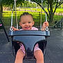 toddler, swing, playground, child, smile, outdoor, park, greenery, chains, black_swing, sunlight, happy, grass, tree, pavement, stroller, person, clothing, feet, legs